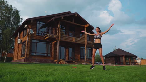 slim beautiful woman in sportswear on the background of the house on the lawn performs jumps for cardio training and fat burning