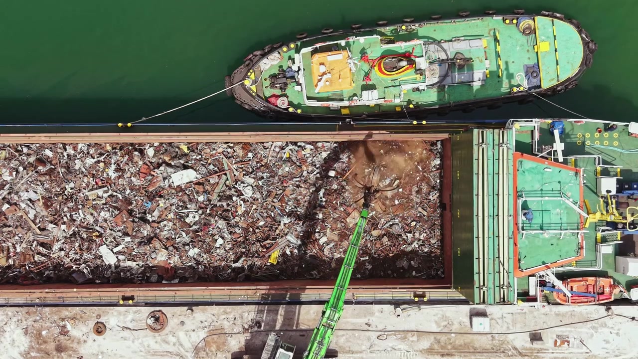 Nave da carico che trasporta rottami nel porto durante le ore diurne con un rimorchiatore che assiste nel processo di carico per il trasporto.