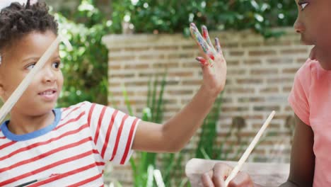 happy african american brother and sister in bunny ears painting eggs for easter, slow motion