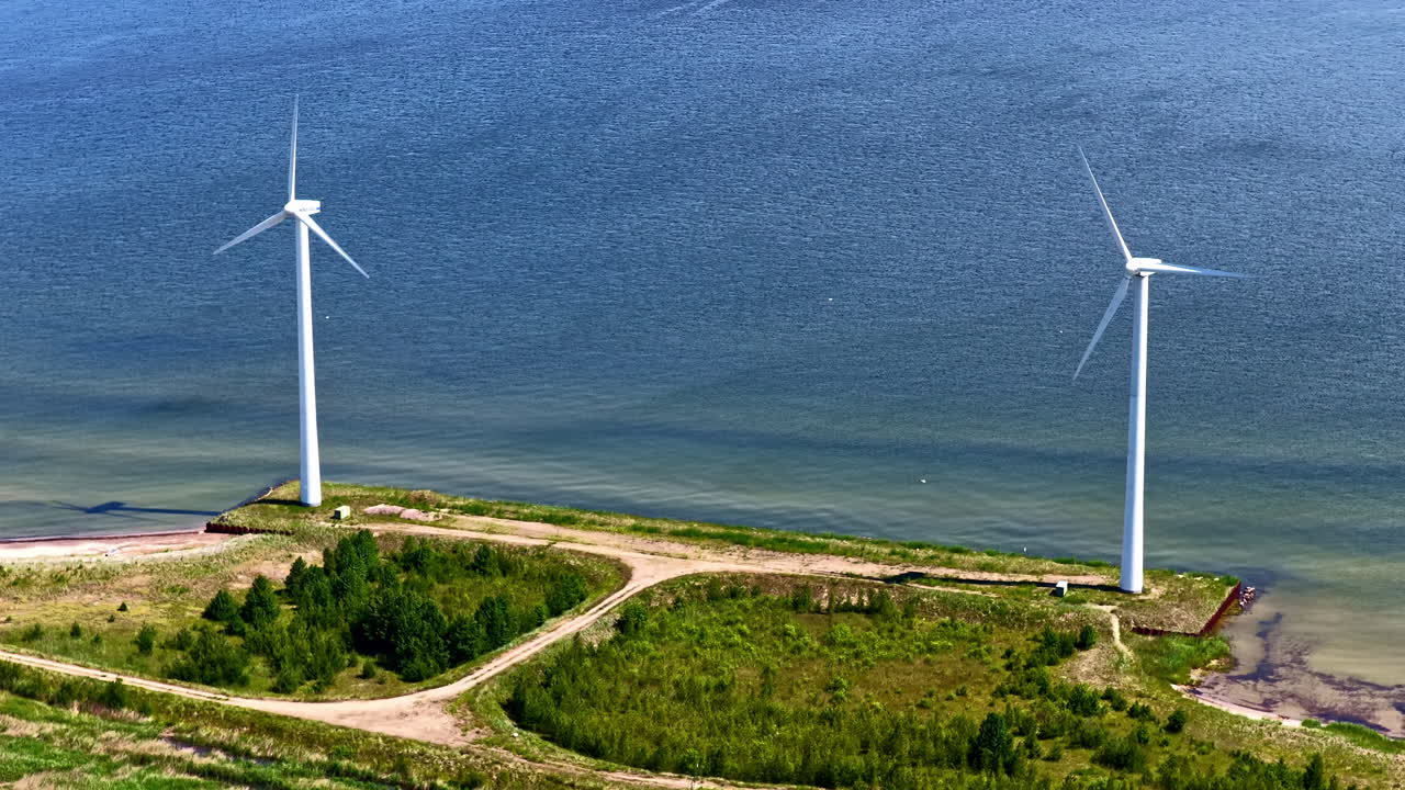 Two wind turbines stand along a grassy coastline, harnessing wind energy near the Baltic Sea. Riga, Latvia