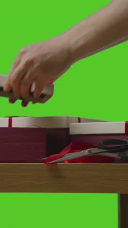 vertical video of man putting present into gift wrapped box on table shot against green screen 3