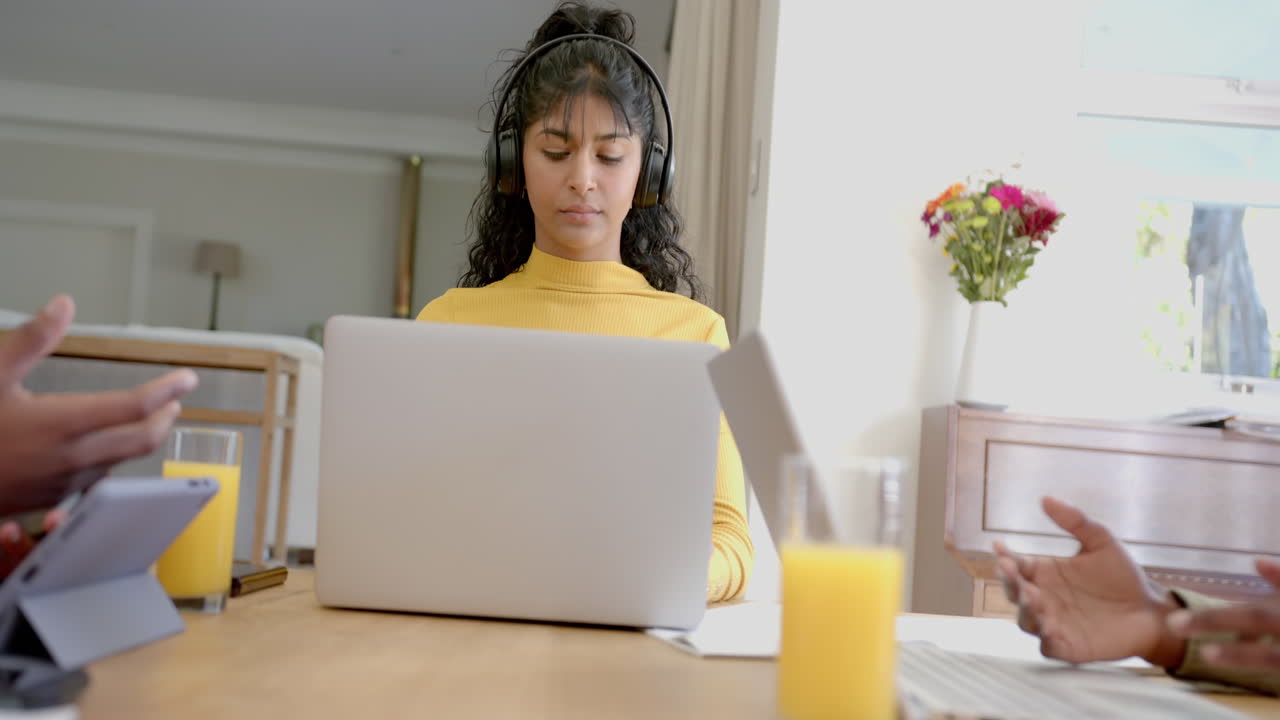 Happy diverse group of teenage friends studying at table with laptops at home, slow motion
