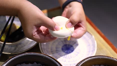 hands opening a steamed bun with filling