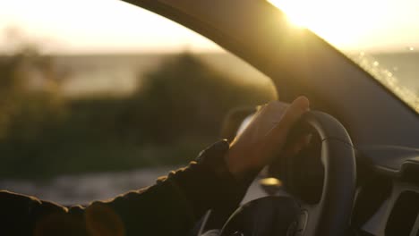 Bearded-man-focusing-driving-a-car-along-the-coast,-golden-hour,-blurred-background