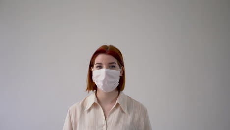 Woman-with-medical-face-mask-and-gloves-pointing-up-an-empty-blank-space.-Copy-space-and-white-background.-Frontal-view.