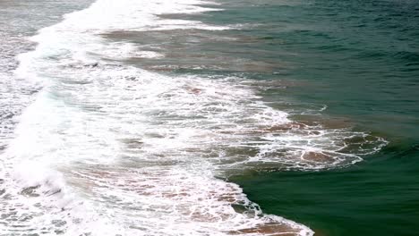 Evening-tide-rolling-in-on-a-sandy-beach,-The-play-of-sunset-light-on-ocean-waves