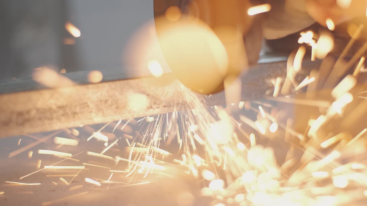 남자는 원형 도자기를 니다. 뜨거운 금속에서 불꽃이 날아갑니다. 남자는 강철 위에서 열심히 일합니다. 차고에서 찍은 클로즈업 느린 동작입니다.