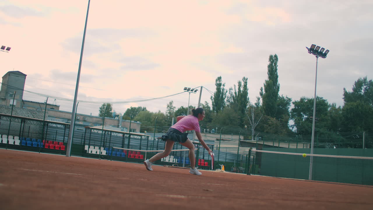 테니스 경기를 준비하는 젊은 여성 테니스 선수의 느린 영상으로 낮은 각도 뷰. 여성 운동 선수가 스포츠 연습 중에 공을 강력하게 때리고 있습니다. 상업적 사용 영상