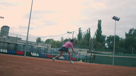 Low-angle-view-in-slow-motion-of-a-young-female-tennis-player-preparing-to-serve-a-tennis-match.-A-woman-athlete-is-powerfully-hitting-a-ball-during-sports-practice.-Commercial-use-footage