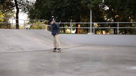 Junger-Skater-In-Lässiger-Kleidung-Und-Schwarzem-Hut,-Der-Von-Der-Rampe-Rutscht-Und-Im-Skatepark-Erfolgreich-Einen-Flip-trick-Mit-Dem-Brett-Macht