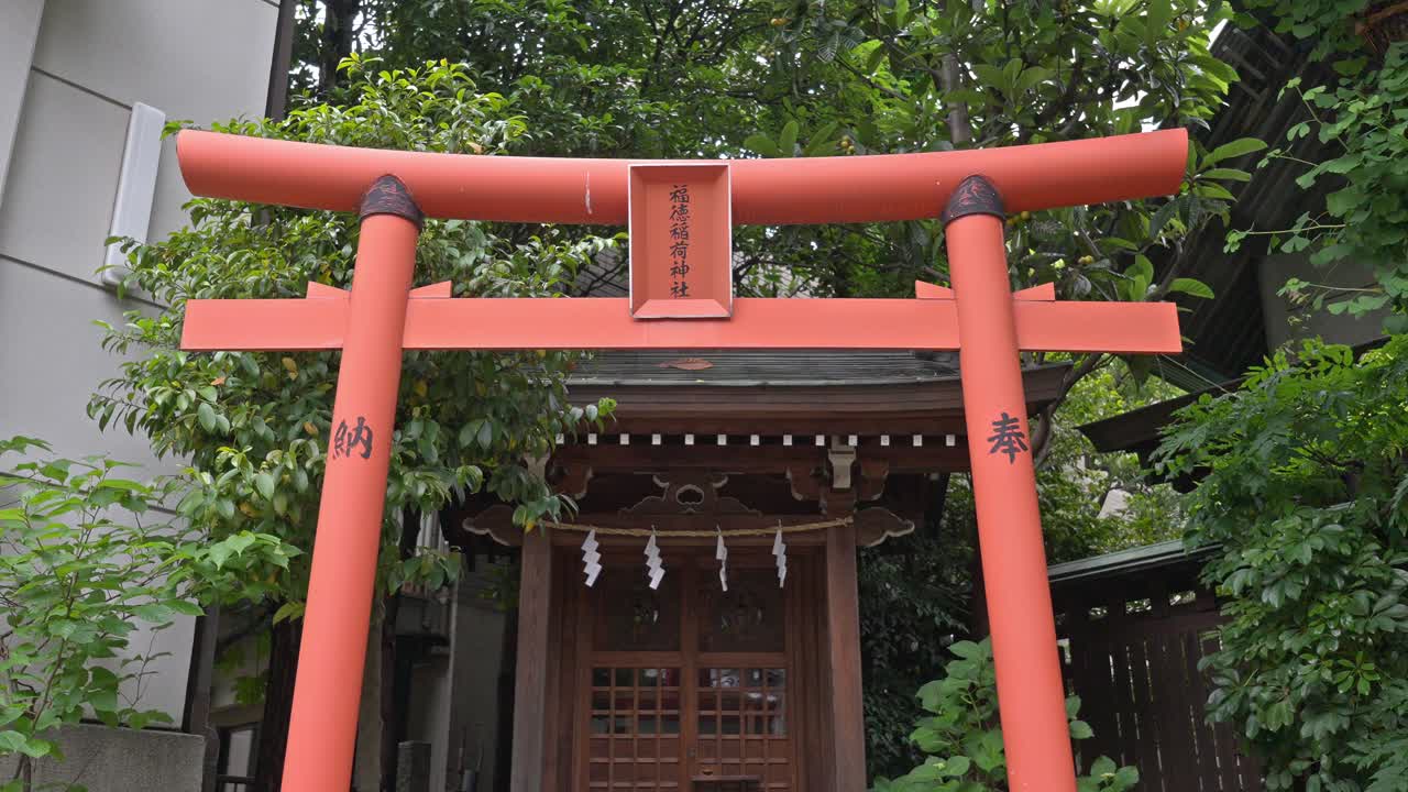 A prominent red torii gate marks the entrance to Kuramae Shrine, a traditional Japanese spiritual site nestled amidst urban surroundings.