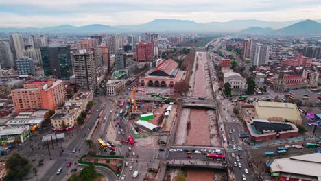 aerial view establishing over the mapocho river and the cultural center mapocho station, construction site and high flow of people, mountains with pollution in the background santiago chile