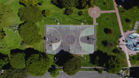 vista de arriba hacia abajo de personas jugando al baloncesto en una cancha de baloncesto de concreto en un parque al aire libre con césped verde y árboles exuberantes