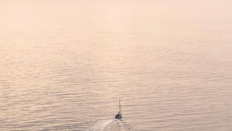 a small sailboat alone in the vast ocean during sunset