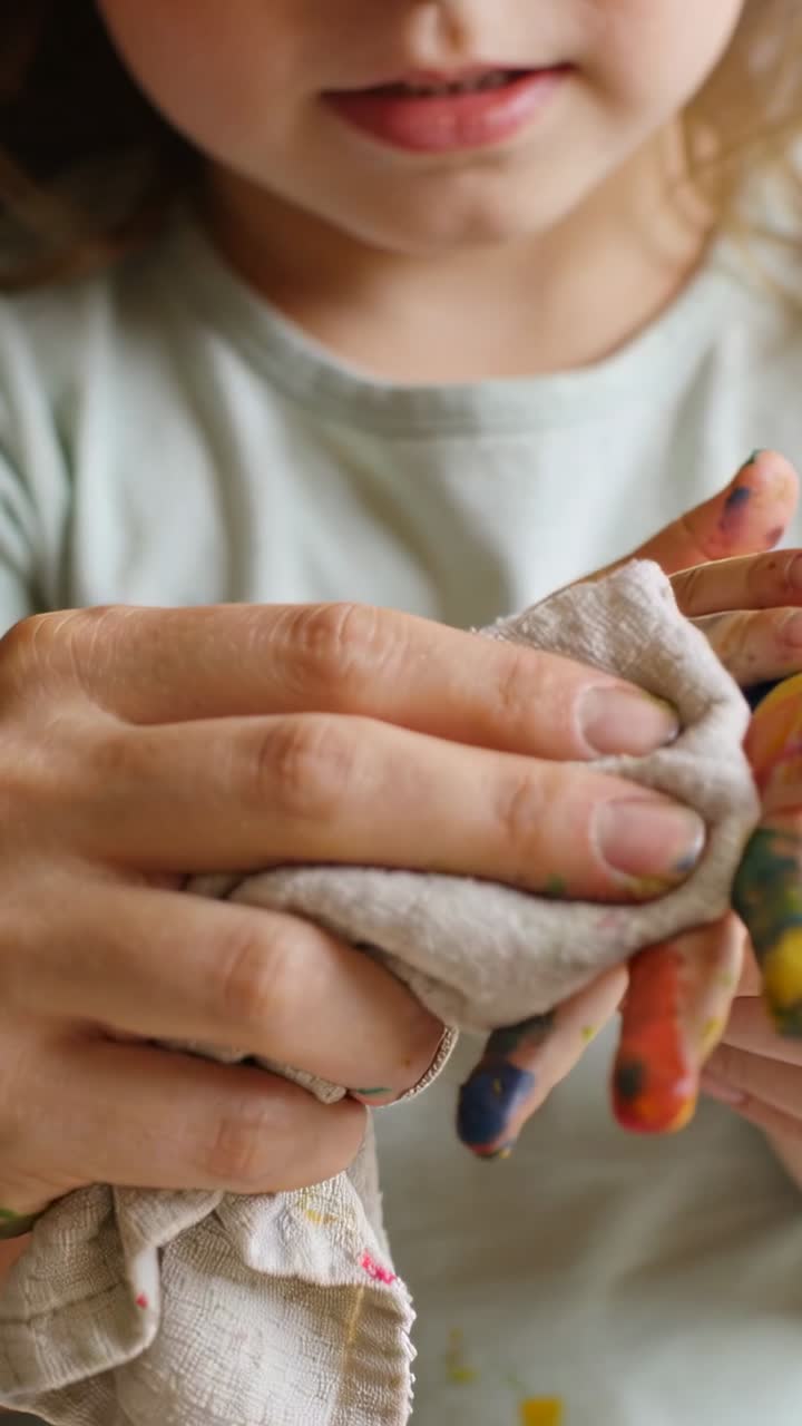Vertical video: Wiping adult cleaning child's painted hand at home after craft, rag removing paint