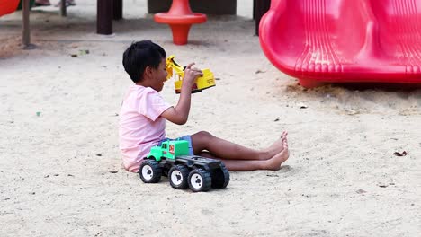 young boy enjoys playing with toy vehicles in sand