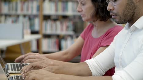 gente pensativa hablando mientras escribe en computadoras portátiles en la biblioteca