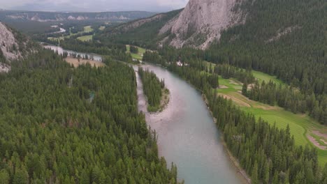 aerial dolly in over bow river between pine forest near steep hill, canadian rockies in back, banff national park, alberta, canada