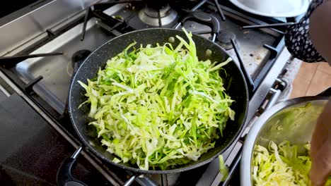 a pan on a stove holds sliced cabbage, showcasing a cooking preparation process.
