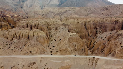 A Scorpio jeep cruises through the rugged mountain desert of Mustang, Nepal, with breathtaking natural structures and landscapes in the background