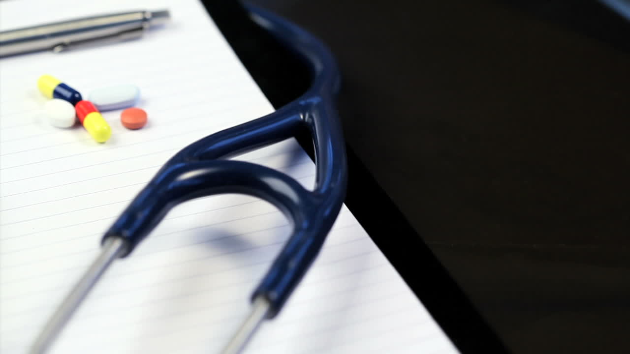 Stethoscope, syringe, pills and pen rotating on a notepad