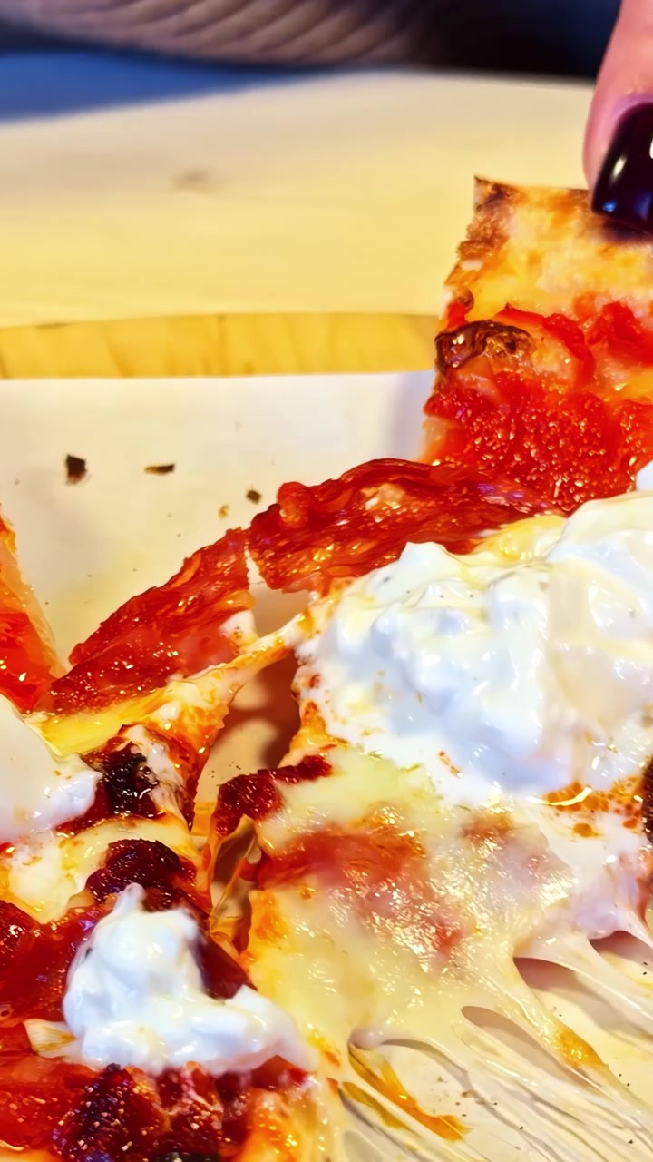 Un primo piano cinematografico di una persona che tira una fetta di autentica pizza italiana condita con burrata fresca e salsa di pomodoro, mostrando il formaggio filante.