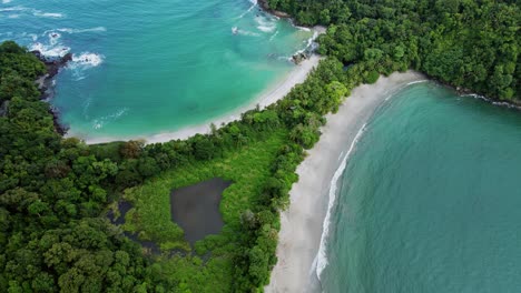 drone flyover tropical blue sea surrounding manuel antonio beach headland with green trees, 4k aerial costa rica