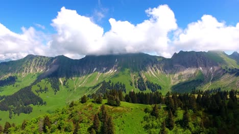 aerial shot over alpine landscape, switzerland in spring forest and alpages, summits in the background in the clouds