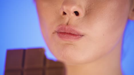 extreme close-up caucasian woman biting a chocolate bar and chews, isolated blue