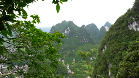 karst mountains surround xingping with scattered houses in a valley, framed by green leaves, china