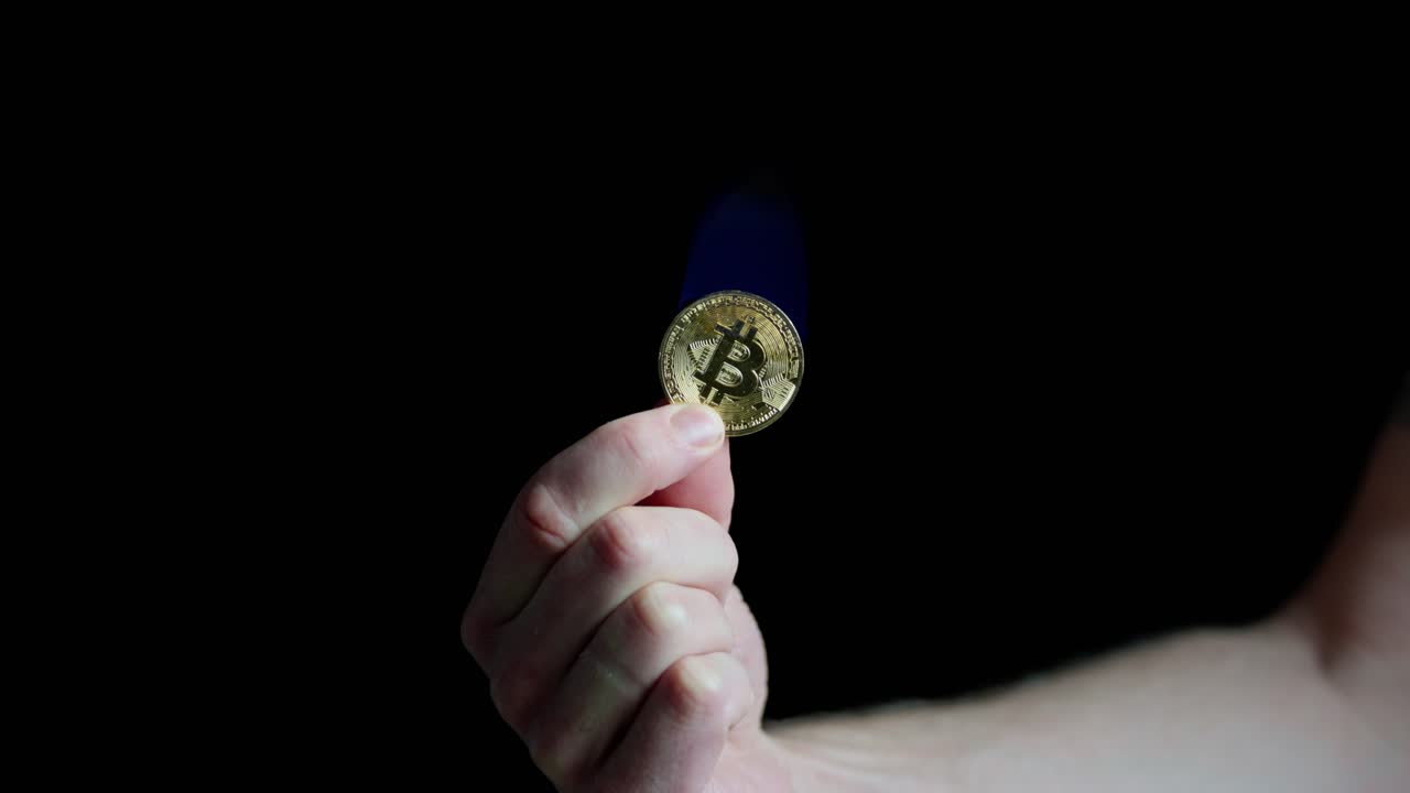 Hand holding bitcoin on fire, blue flame burning on black background, slow push in.