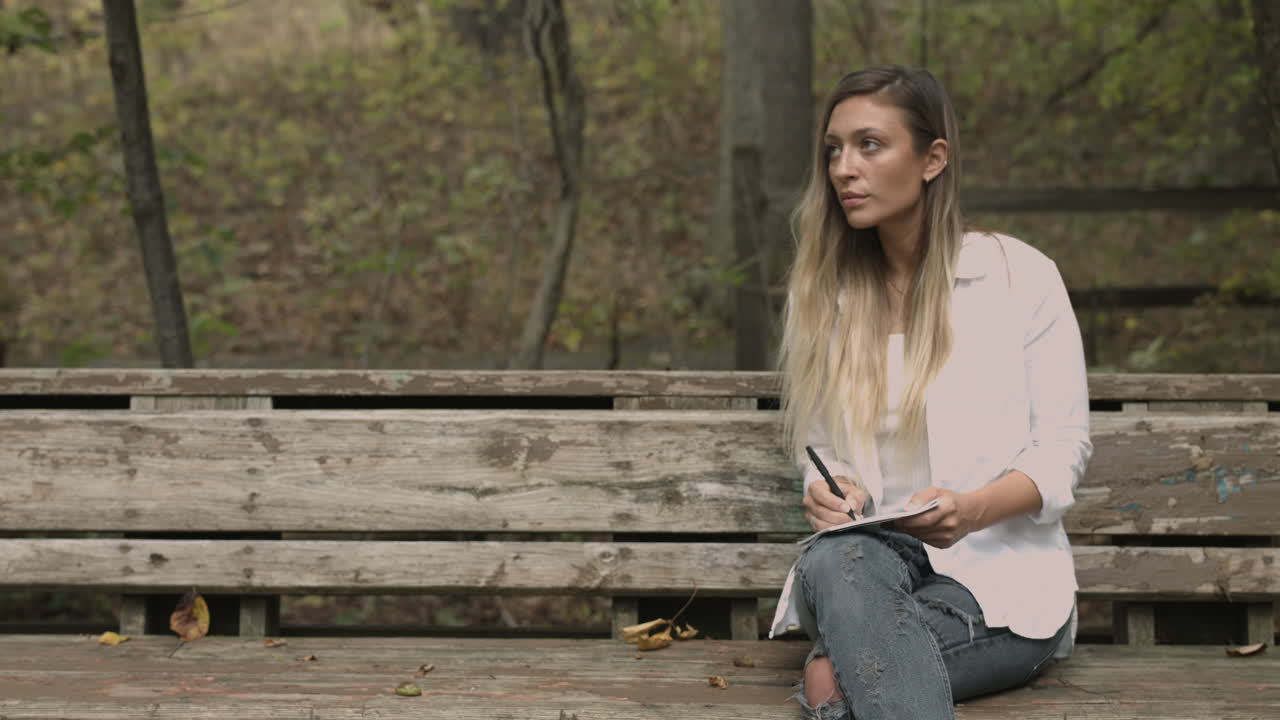 Young college aged woman sits in a forest and draws sketches takes notes slider dolly shot