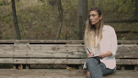 young college aged woman sits in a forest and draws sketches takes notes slider dolly shot