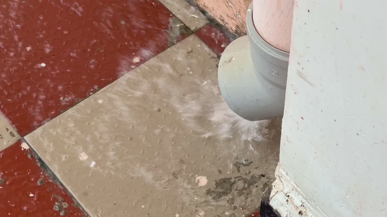 A closeup of water exiting a gutter pipe shows rainwater actively flowing out of the downspout