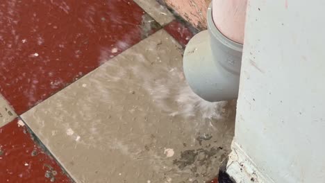 a closeup of water exiting a gutter pipe shows rainwater actively flowing out of the downspout