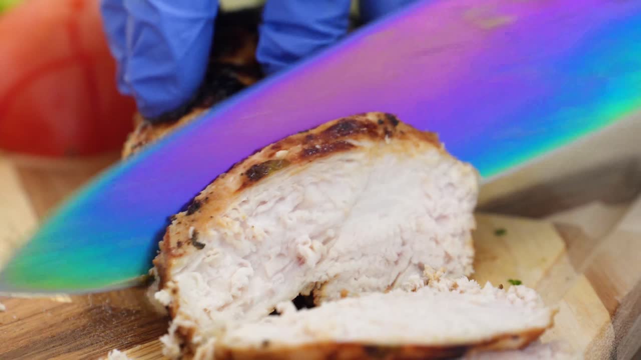 Slicing thin portions of roasted chicken with a big knife while wearing rubber gloves, closeup of hands and cutting board for chopping mean