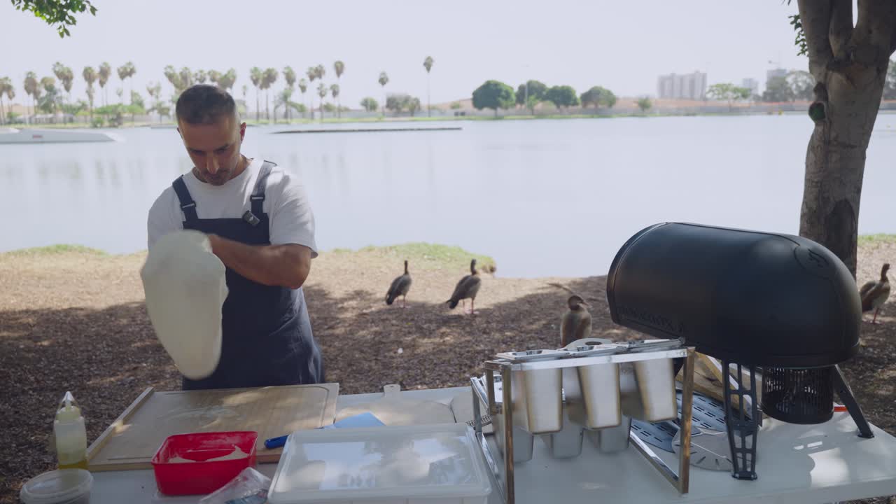 Neapolitan pizza preparation outdoors chef stretching dough by lake portable gas oven ready scenic park location water view