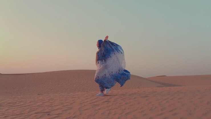 mulher de vestido tradicional a caminhar no deserto ao pôr-do-sol