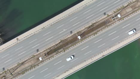 aerial top down view of high way bridge over the ocean see with slow motion of urban traffic car and flock of white birds
