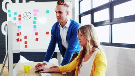 Businesswoman-interacting-with-man-while-working-on-computer