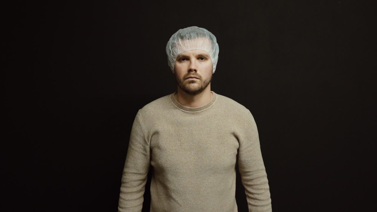 Un uomo indossa una cuffia per capelli usa e getta su uno sfondo scuro. Idea di protezione dei capelli, conformità igienica e standard di sicurezza nell'industria, nella produzione alimentare o negli ambienti medici.