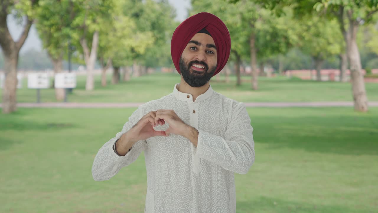 Felice uomo Sikh indiano che fa il segno del cuore nel parco