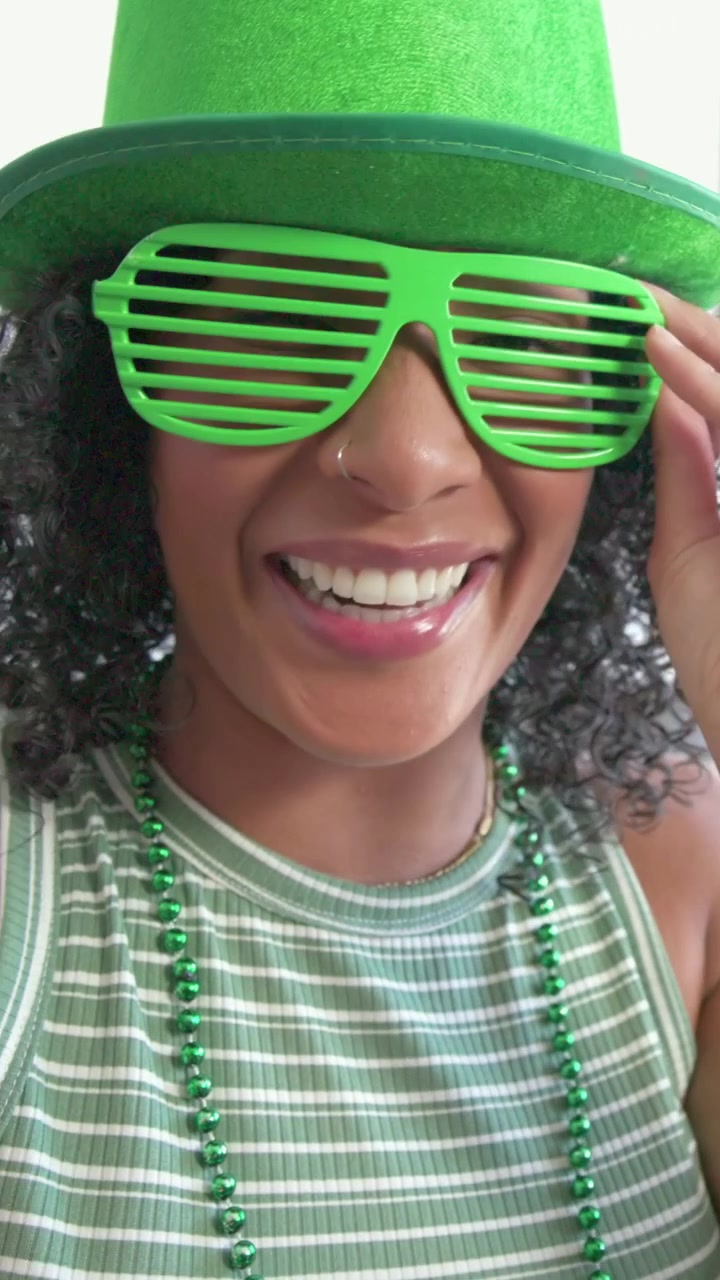 Vertical video: Tapping record, woman fixing green hat and shutter shades on sofa, filming selfie