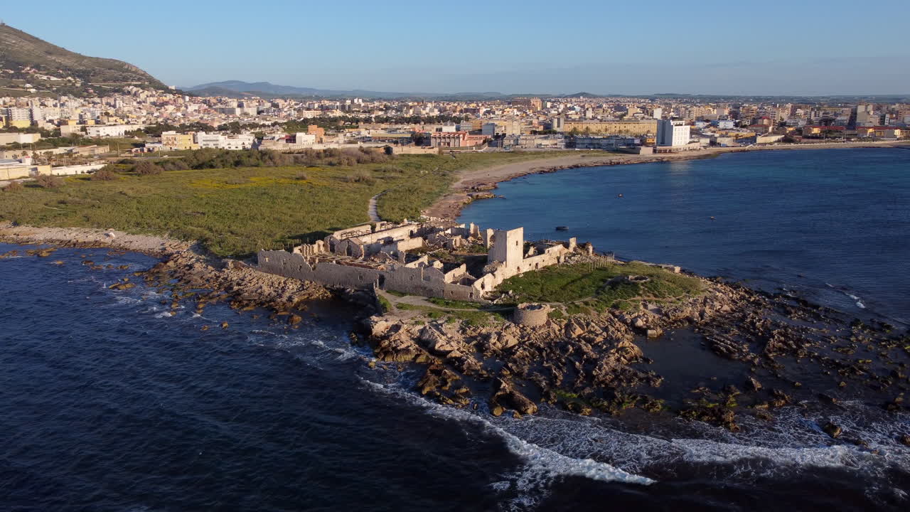 Ripresa aerea circolare della tonnara di San Giuliano al tramonto. Trapani sullo sfondo, Italia.