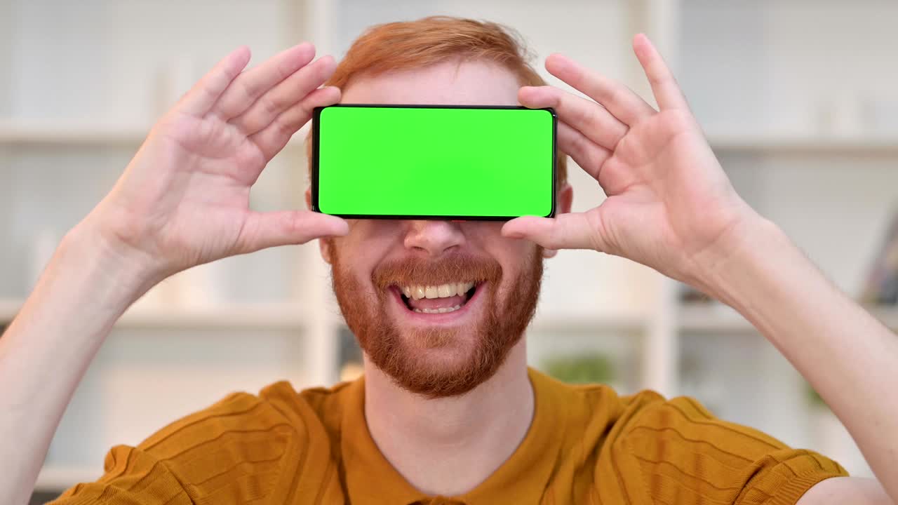 retrato de un hombre pelirrojo alegre con un teléfono inteligente con pantalla cromada sobre los ojos