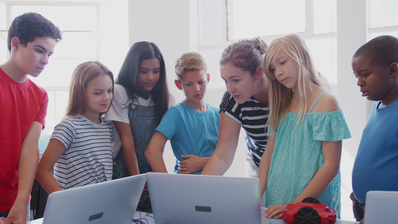 Students With Female Teacher In After School Computer Coding Class Learning To Program Robot Vehicle