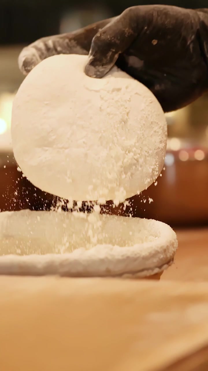 Primo piano delle mani di uno chef con guanti neri che impastano l'impasto artigianale per pizza con la farina