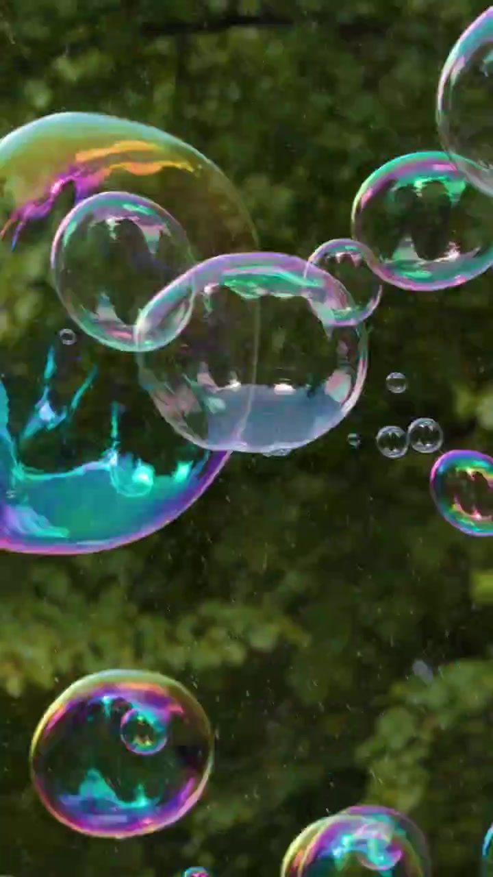 Colorful iridescent soap bubbles drift through the air against a blurred green forest background