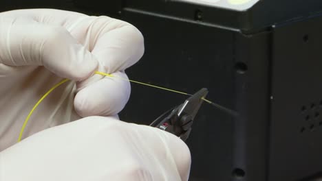 hands with gloves stripping a fiber optic cable with a wire stripper removing the coating of the fibre line