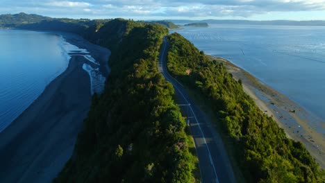 aerial drone fly above asphalted avenue through green island hills at patagonian sea, chiloé, chile, travel destination, lemuy island connection with detif